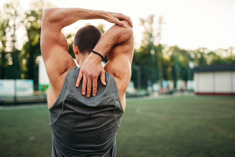 A man performs a triceps stretch on a sports field, promoting flexibility and joint health. - Hastings Chiropractic